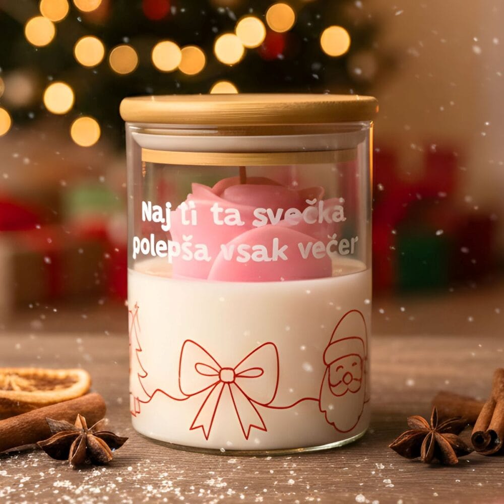 Božična dišeča sveča z napisom "Naj ti ta svečka polepša vsak večer" z roza vrtnico, postavljena v praznično dekoracijo ob začimbah in božičnem drevescu.