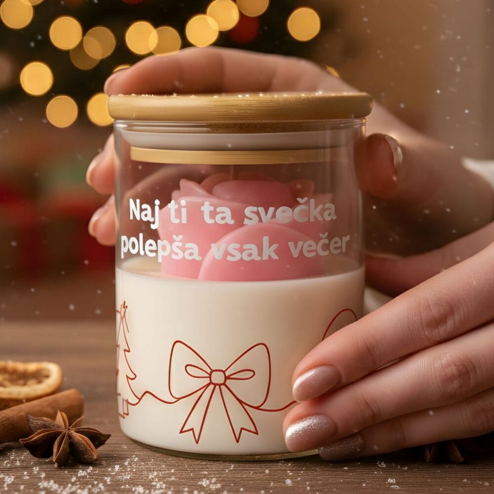 Roke držijo dišečo svečo darilo z napisom "Naj ti ta svečka polepša vsak večer", z roza vrtnico in božičnim motivom, na leseni mizi z začimbami in zamegljenim božičnim drevescem v ozadju.