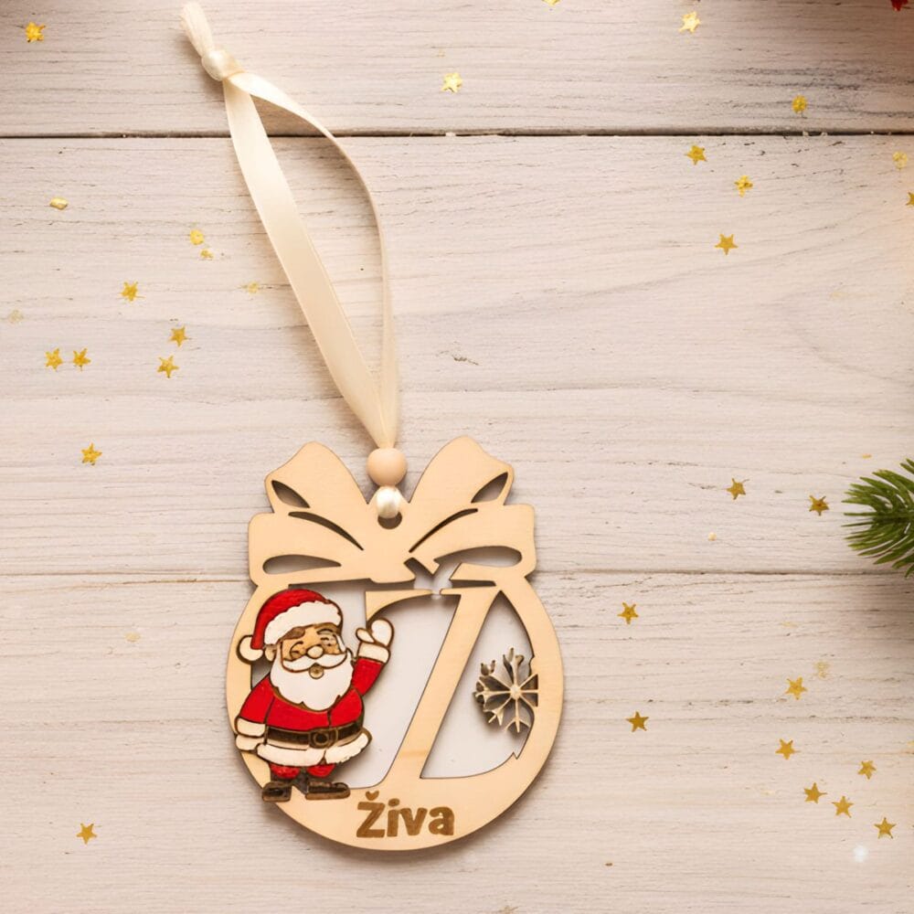 Leseni personaliziran božični okrasek z motivom Božička, izrezljano črko 'Ž' in imenom 'Živa', položen na svetli leseni podlagi z zlatimi zvezdicami.