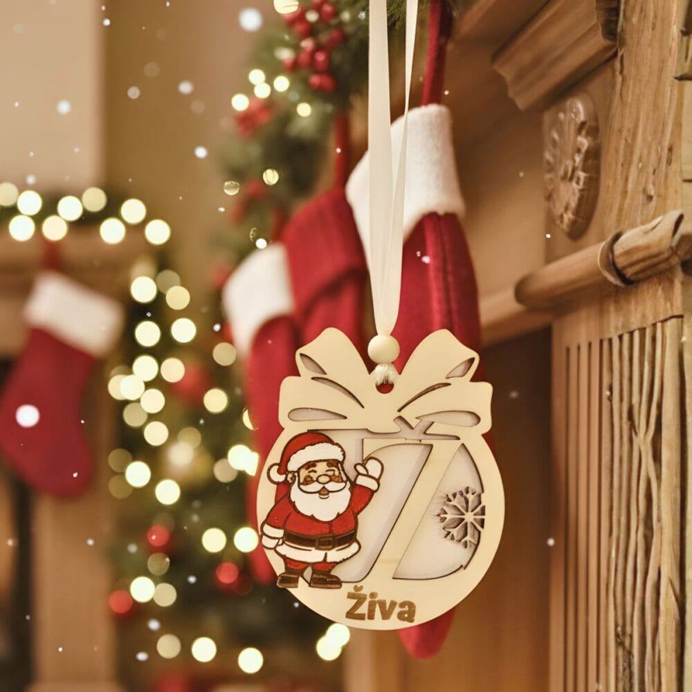 Leseni personaliziran božični okrasek z motivom Božička, izrezljano črko 'Ž' in imenom 'Živa', obešen na kaminu s praznično dekoracijo v ozadju.