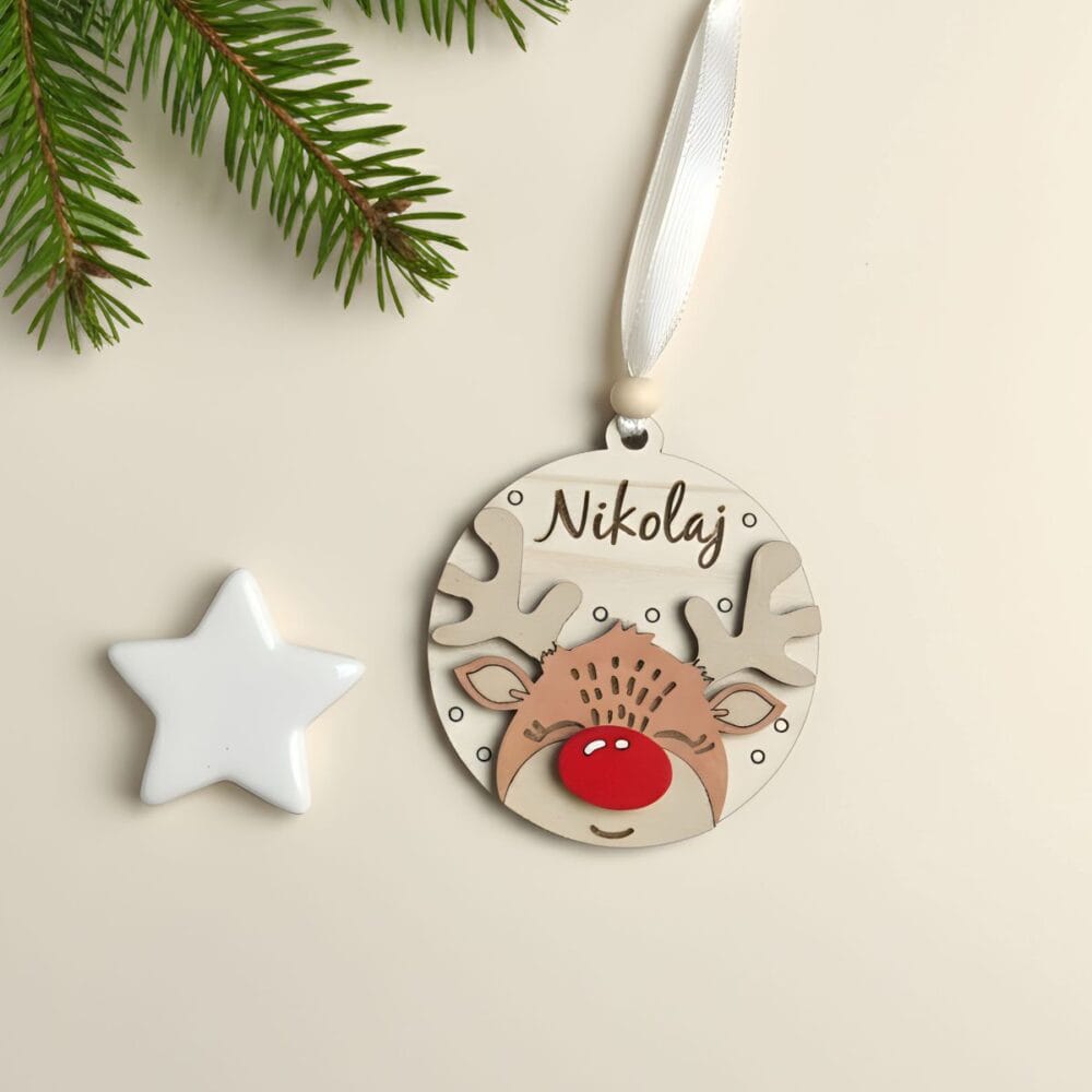 Leseni personaliziran božični okrasek Jelenček z rdečim noskom in imenom 'Nikolaj', na bež ozadju z belo zvezdo in smrekovo vejico