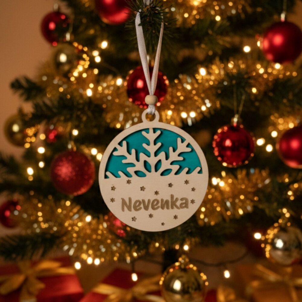 Dvoslojni personaliziran okrasek Snežinka z vgraviranim imenom 'Nevenka' in zeleno barvno podlago, obešen na božični jelki z rdečimi bunkicami
