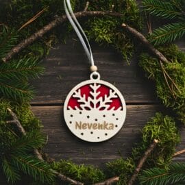 Dvoslojni personaliziran okrasek Snežinka z rdečo podlago in imenom 'Nevenka', postavljen v krog naravne dekoracije iz mahu, vejic in borovih iglic