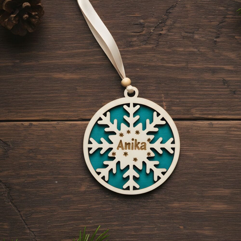 Personaliziran božični okrasek iz lesa, snežinka, zeleno ozadje, vgravirano ime Anika, na temni leseni podlagi.