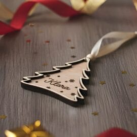 Personaliziran lesen božični okrasek Smrekica z zvezdicami, pripravljen kot praznično darilo, z elegantno pentljico in toplim prazničnim ozadjem.