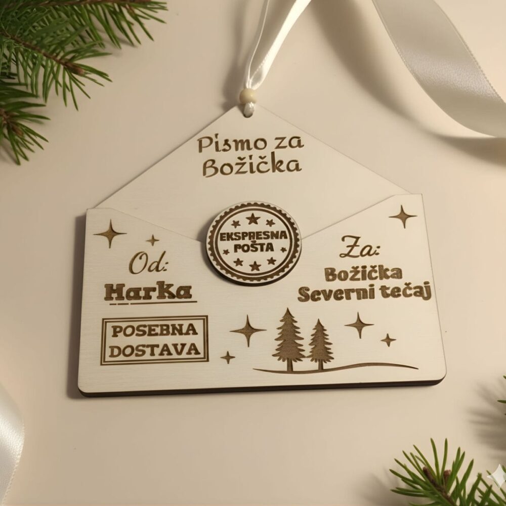 Leseni personaliziran okrasek v obliki kuverte z napisom 'Pismo za Božička' in 'Od: Harka', z žigom 'Ekspresna pošta', položen na svetlem ozadju s smrekovimi vejicami