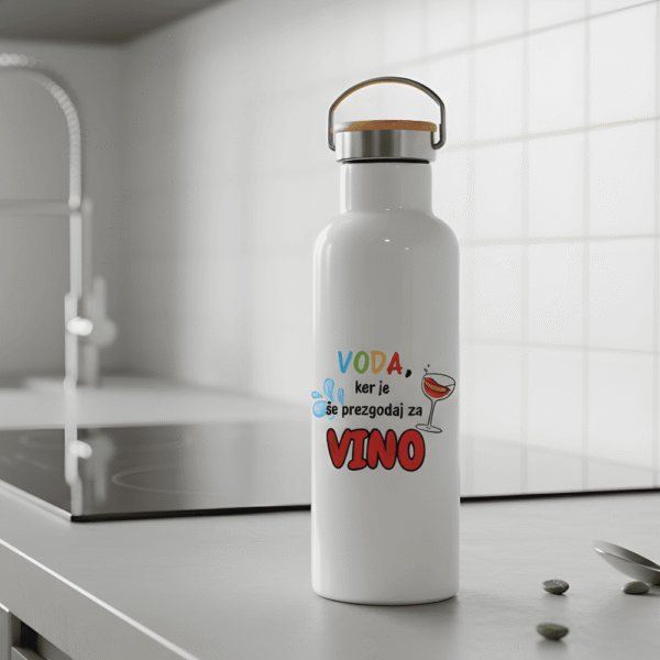 Beli termo bidon Voda | Vino Termovka s šaljivim napisom v sodobni beli kuhinji. Prikaz termovke na kuhinjskem pultu poleg indukcijske plošče. Odlično darilo za ljubitelje vina.
