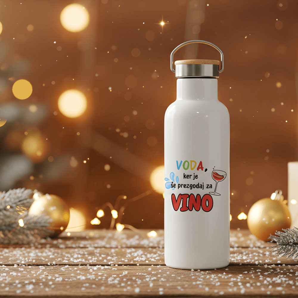 Termovka na leseni mizi, okrašeni z božičnimi lučkami, smrečnimi vejami in zlatimi okraski. Beli termo bidon z napisom "VODA, ker je že prezgodaj za VINO" – idealno Božično darilo ali darilo za Miklavža.