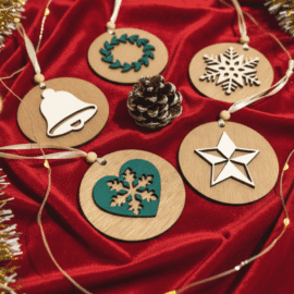 et petih lesenih božičnih okraskov na rdečem žametu. Okraski vključujejo motive zvončka, venčka, snežinke, srca s snežinko in zvezde, obdane z božičnimi lučkami in borovim storžem