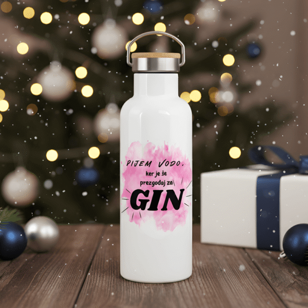 Praznična Termovka Gin O'Clock z napisom "Pijem Vodo, ker je že prezgodaj za GIN" in rožnatim ozadjem. Termo bidon na leseni mizi pred božičnim drevescem, idealno darilo za ljubiteljico gina.