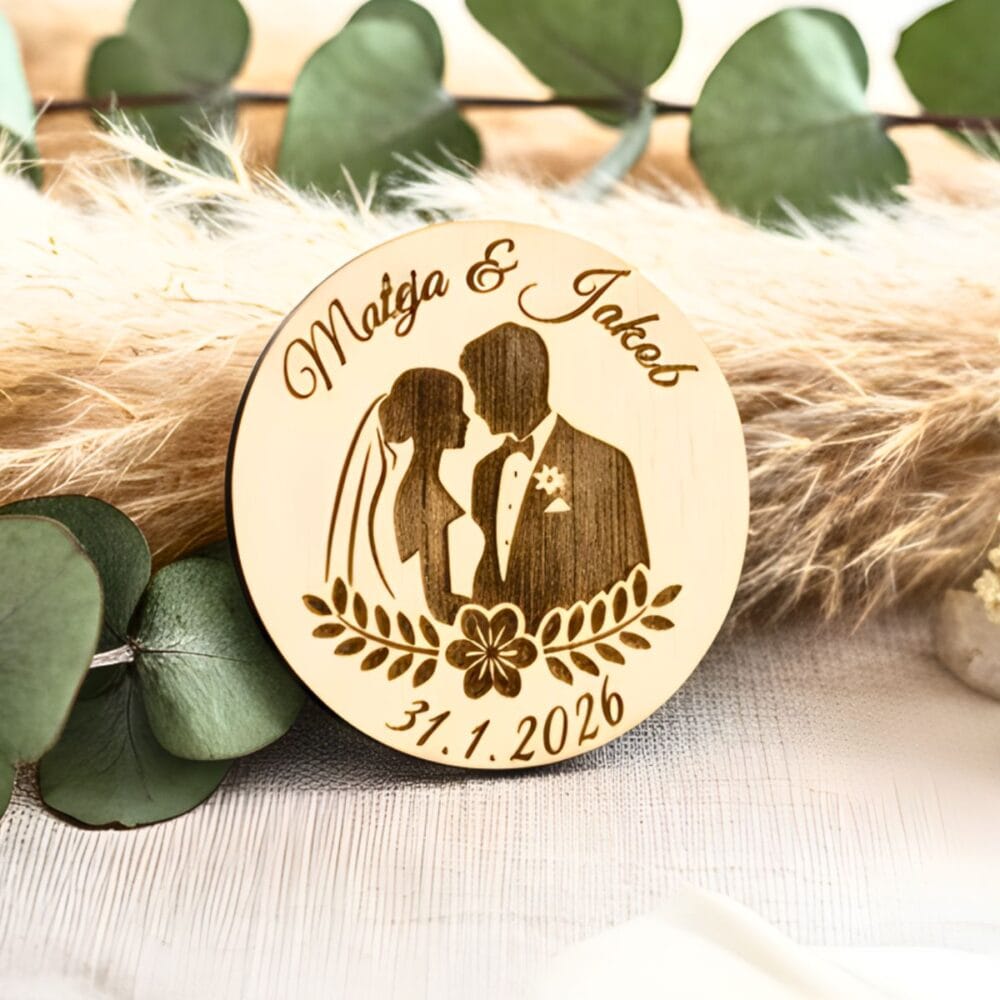 Personaliziran okrogel lesen poročni naprsnik z vgravirano silhueto neveste in ženina, imenoma Mateja & Jakob ter datumom, postavljen na dekorativno pampas travo in evkaliptus.
