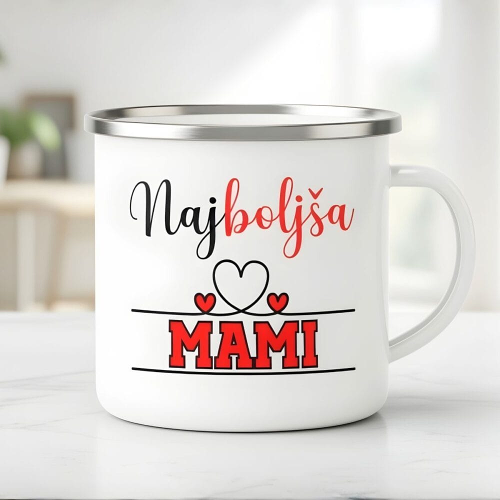 Bel emajliran lonček za mamo s srebrnim robom, ki prikazuje minimalističen napis 'Najboljša MAMI' z rdečimi srčki na svetlem, zamegljenem ozadju kuhinje.
