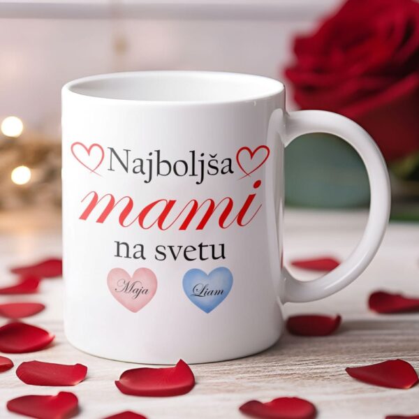Personalizirana bela skodelica z napisom Najboljša mami na svetu, dvema srčkoma z imenoma Maja in Liam, obdana z rdečimi cvetnimi listi vrtnic.