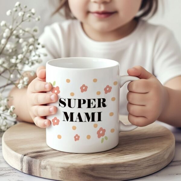 Otrok v rokah drži keramično skodelico z napisom Super mami in cvetličnim vzorcem, kar prikazuje prisrčno darilo za materinski dan.