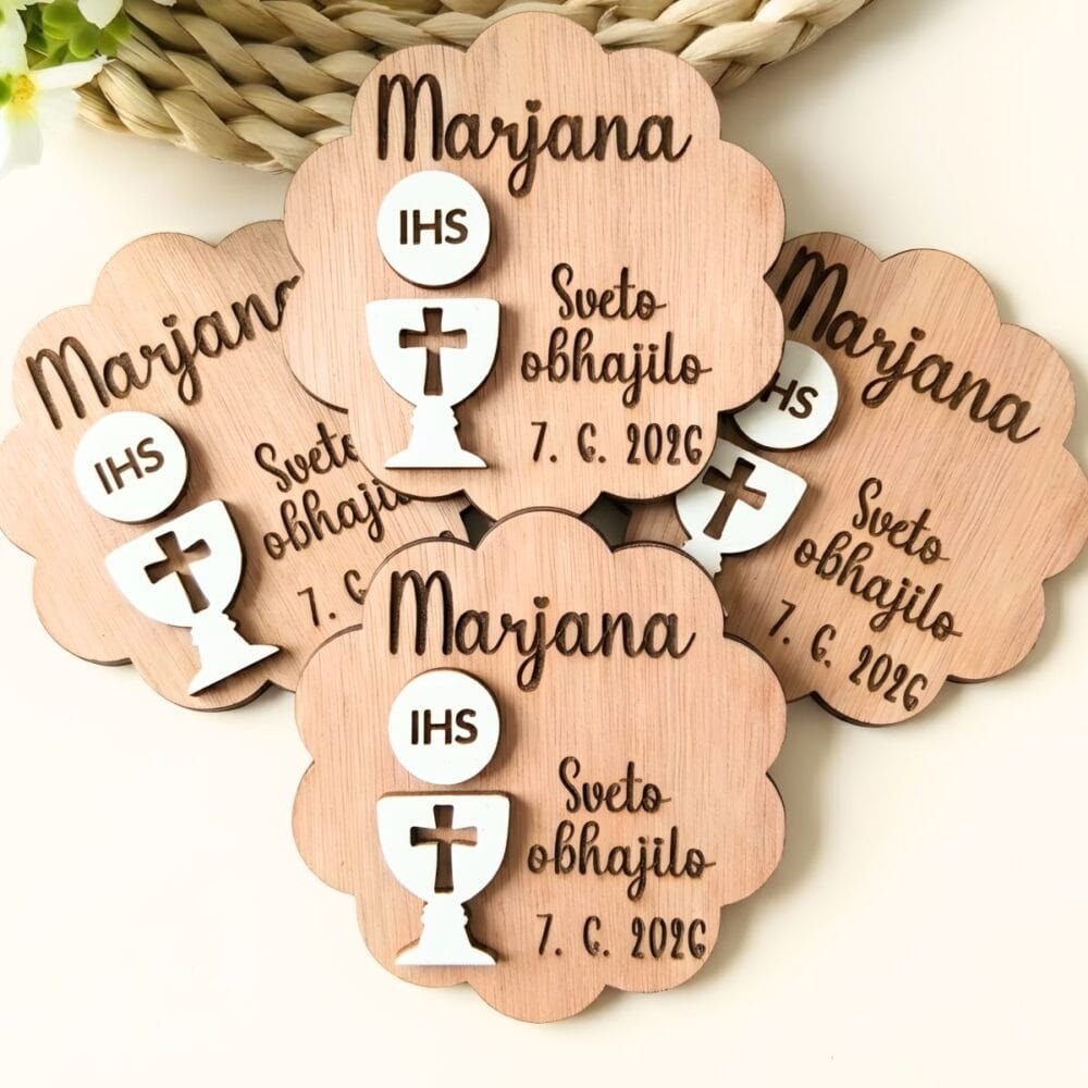 Set personaliziranih lesenih magnetov za prvo sveto obhajilo z reliefnim belim kelihom in hostijo z napisom IHS. Magneti v obliki oblačka vključujejo vgravirano ime Marjana in datum, razporejeni pa so na svetli podlagi ob pletenem podstavku.