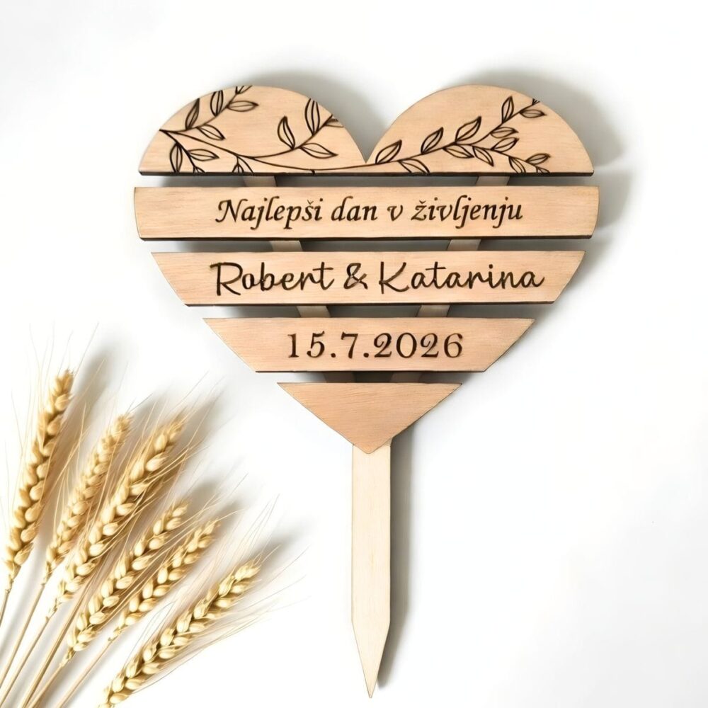 Leseni poročni topper za torto v obliki srca z vgraviranimi oljčnimi vejicami, napisom "Najlepši dan v življenju", imenoma Robert & Katarina ter datumom poroke, obdan s klasjem pšenice.