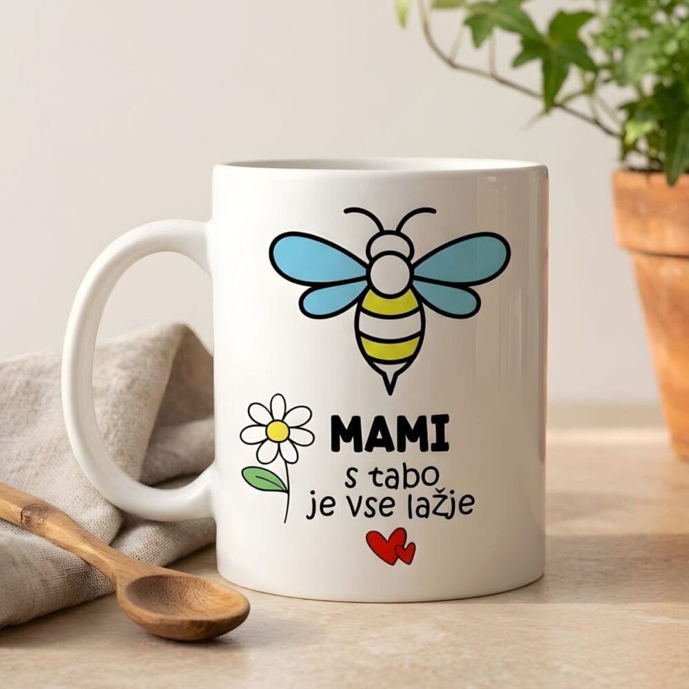Skodelica za mami s čebelico in napisom "MAMI, s tabo je vse lažje", fotografirana v svetlem ambientu ob lončnici v glinenem lončku in leseni žlički na bež podlagi.