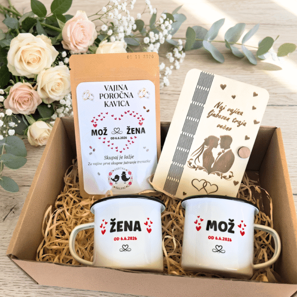 Darilni paket za mladoporočenca, ki vsebuje personalizirani emajlirani skodelici Mož in Žena, poročno kavo in gravirano leseno darilo, v ozadju pa je šopek vrtnic.
