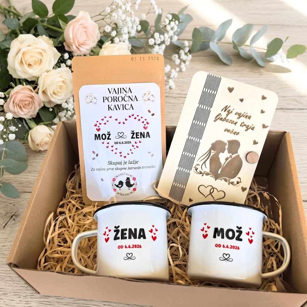 Darilni paket za mladoporočenca, ki vsebuje personalizirani emajlirani skodelici Mož in Žena, poročno kavo in gravirano leseno darilo, v ozadju pa je šopek vrtnic.