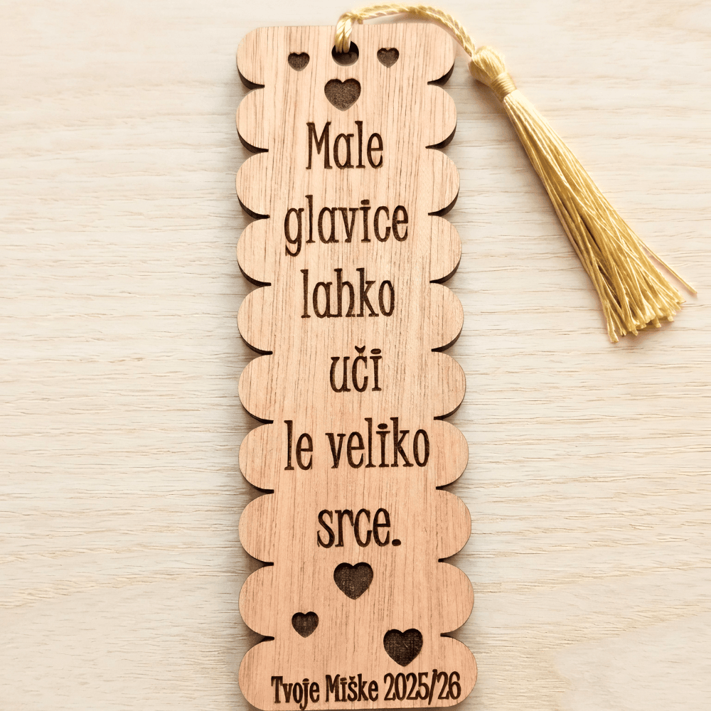 Gravirano leseno kazalo z valovitim robom, izrezljanimi srčki in elegantnim rumenim cofom na nevtralni leseni podlagi kot darilo ob koncu šolskega leta.