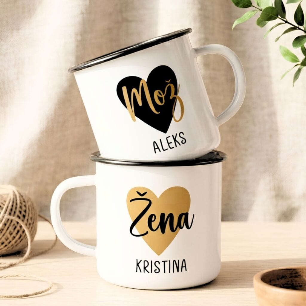 Dve beli emajlirani skodelici s črnim robom, ena položena na drugo. Spodnja skodelica ima zlato srce z napisom »Žena« in imenom »KRISTINA«, zgornja pa črno srce z napisom »Mož« in imenom »ALEKS«. Skodelici stojita na leseni podlagi ob lesenem kolutu z vrvico.