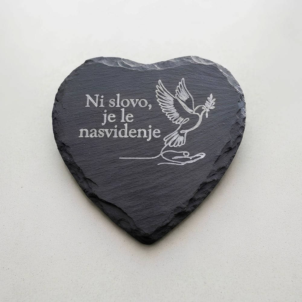 Spominski kamen v obliki srca iz črnega skrilavca z belo gravuro dlani, goloba in napisom Ni slovo, je le nasvidenje