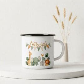 Beli emajlirani lonček s črnim robom in personaliziranim napisom "Nikolaj" pod nizom barvnih trikotnih zastavic. Na sredini lončka je risana ilustracija safari živali: žirafa, velik slon, majhen slon, ptica in lev, obdani z zelenim listjem. Lonček stoji na belem podstavku v svetlem prostoru, v ozadju pa je vaza s suhimi klasjem.